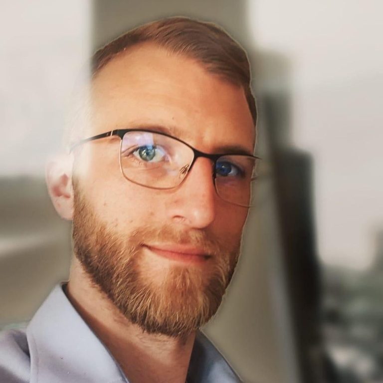Michael Böhm mit Brille und kurzem Bart, lächelnd vor einem unscharfen Hintergrund.